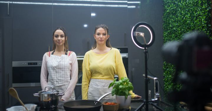 Culinary Demos - Two Young Women Standing behind the Counter with Cooking Appliances in front of a Camera