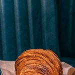 Culinary Demos - Tasty freshly baked croissant on parchment paper placed on dark leather sofa in daylight